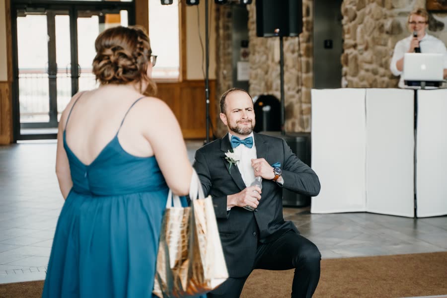 A groomsman kneeling with a gift at the reception